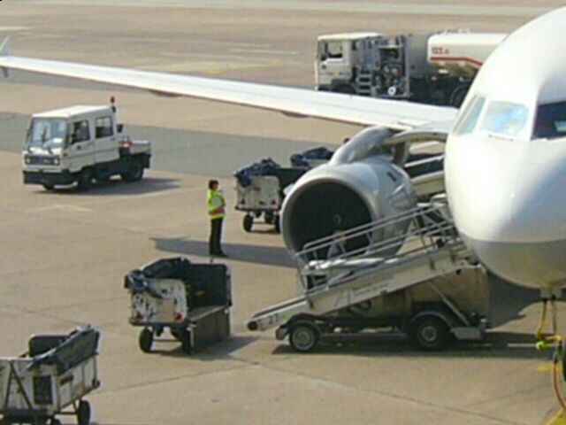 A loading platform and container dollies are positioned beside an airliner on the apron.