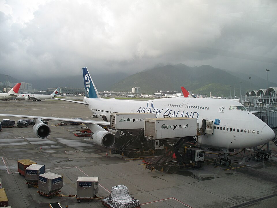 Two raised catering trucks stand beside a widebody airliner, with wheeled cargo containers across the foreground.