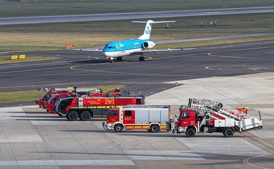 Several airport fire and rescue vehicles are parked near an airliner and airfield movement areas.