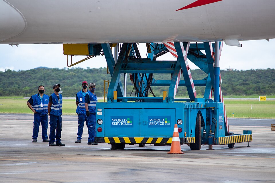 Ground crew beside a blue scissor-lift cargo platform raised beneath a large aircraft fuselage.