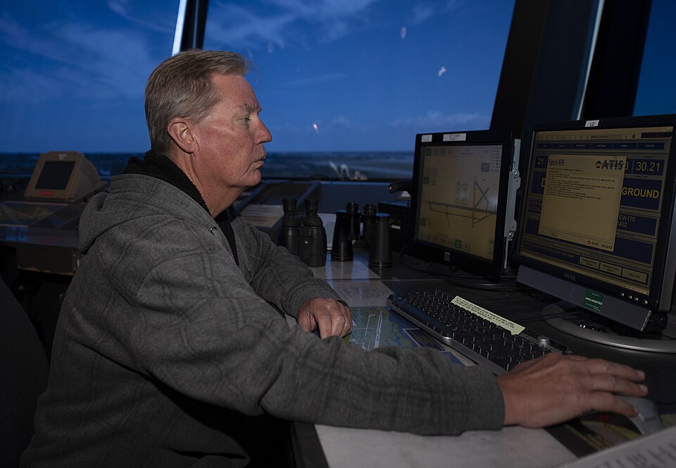 Controller seated at several computer screens inside a glazed airport tower.