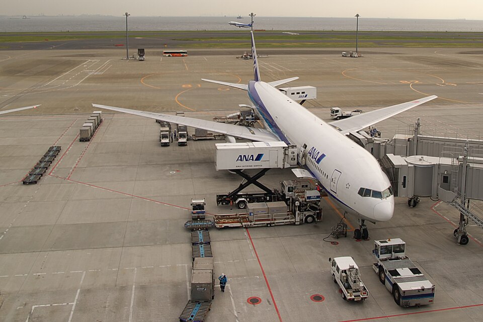High-angle view of an ANA airliner surrounded by service vehicles and a passenger bridge.