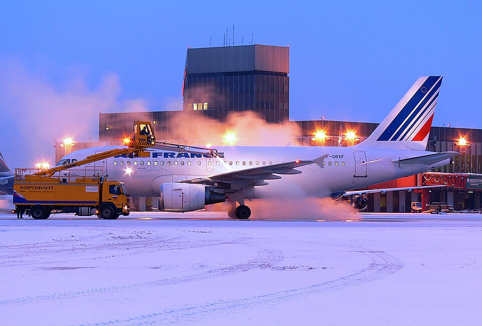 Air France airliner surrounded by spray and elevated service equipment on a snow-covered apron.