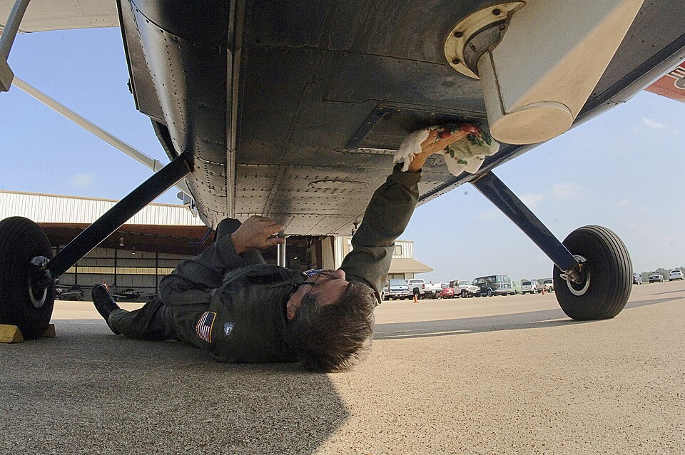 Person beneath a light aircraft wiping a small glass panel on the underside of its fuselage.