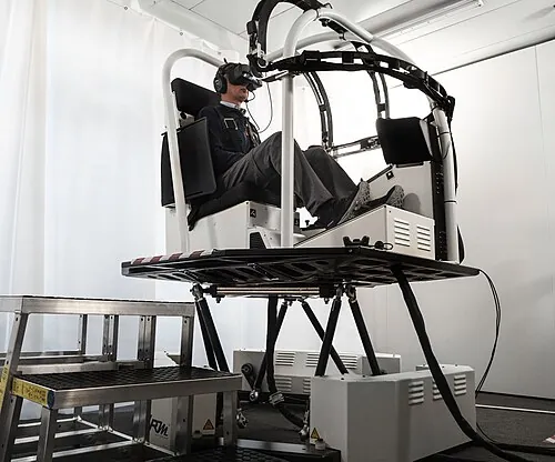 An open helicopter training device with a seat and controls on a motion base.
