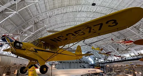 A yellow Piper J-3 Cub displayed in an aviation museum.