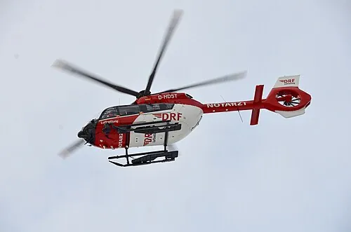 A red-and-white air-ambulance helicopter flying against a pale sky.