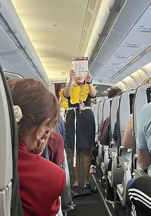 A person demonstrating safety equipment in an aircraft cabin.
