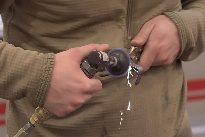 A structural technician uses a pneumatic grinder on a component.