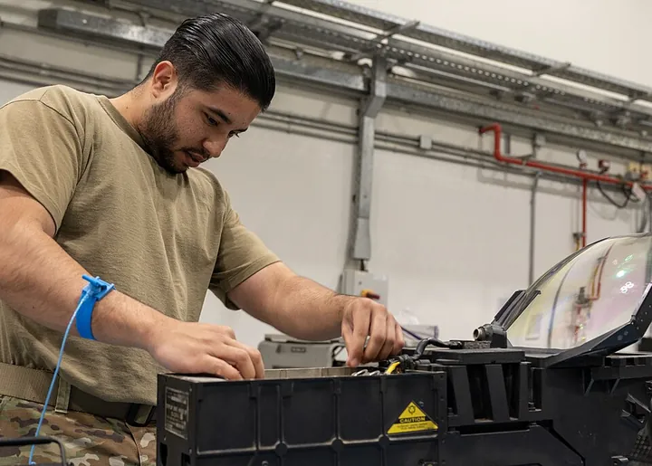 An avionics technician examines electronic equipment on a workbench.