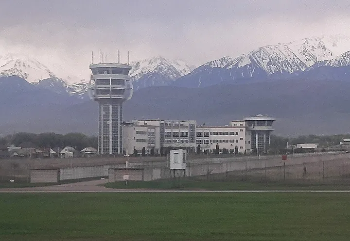 Air traffic control tower at Almaty International Airport, with mountains in the background.
