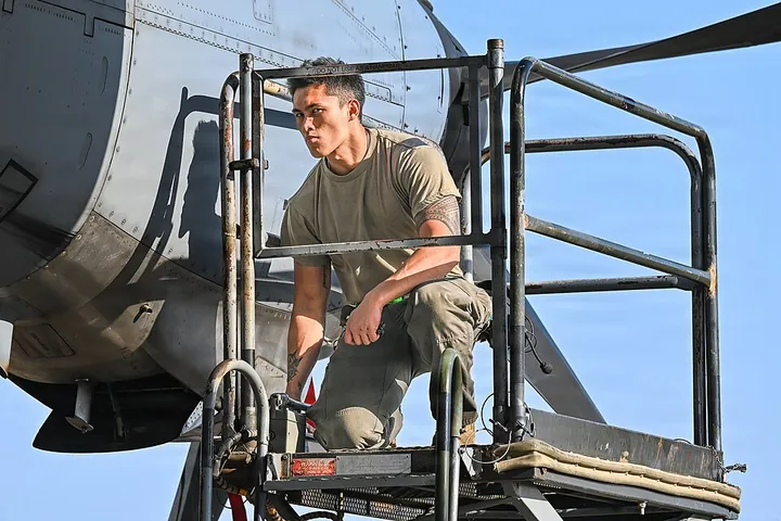 A technician raises a maintenance stand beside a C-130.