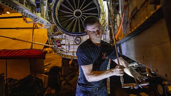 Engine maintenance takes place on an MH-60R helicopter inside a hangar.