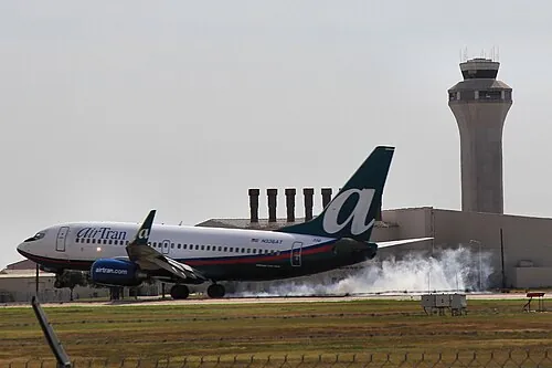 AirTran Boeing 737 at touchdown with a control tower behind it.
