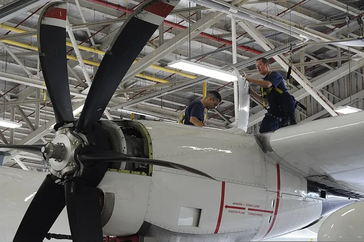 Maintenance personnel lift an engine cowling to reach the equipment beneath it.