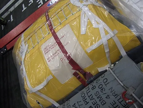 A tightly packed yellow evacuation-slide unit wrapped in protective material.