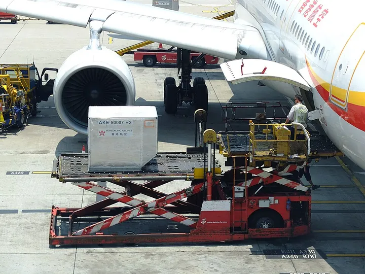 A loader raising a unit load device from apron-dolly height toward an aircraft cargo door
