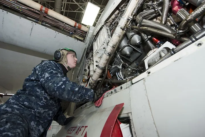 A technician services the hydraulic system of a C-2A in a hangar.