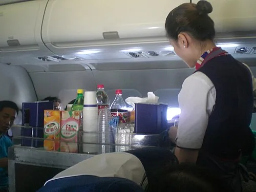 An aircraft cabin with a crew member and passenger seating.