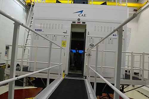 A large enclosed flight simulator on support legs inside a building.