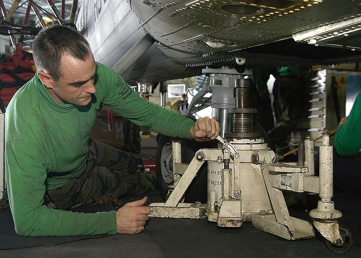 A technician adjusts a hydraulic jack beneath a helicopter.