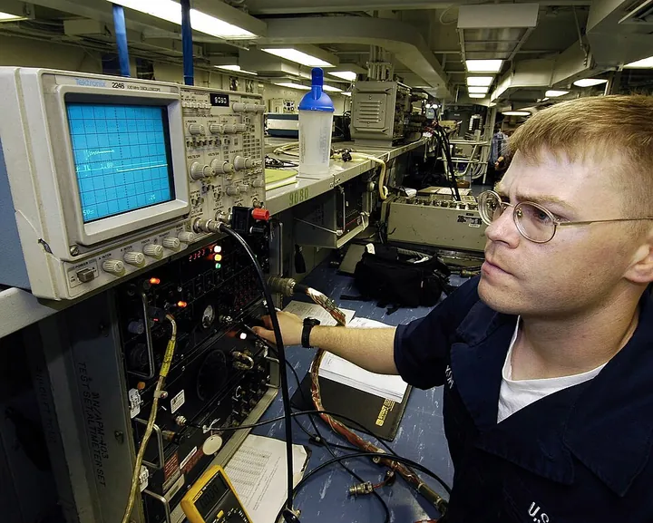 A technician uses an oscilloscope to check signals in avionics equipment.