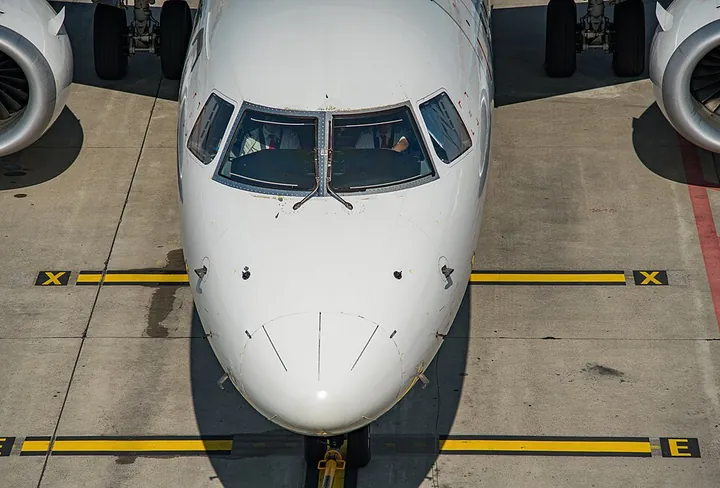 Front view of an airliner with pilots visible through its cockpit windows.
