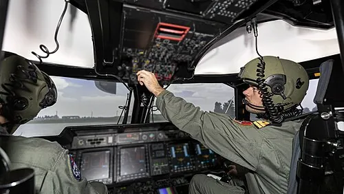 People seated at the controls inside an NH90 helicopter simulator.