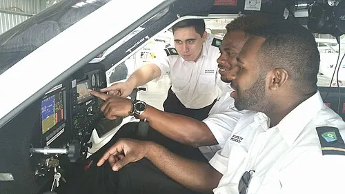 People seated together in an aircraft cockpit, with one pointing toward the controls.