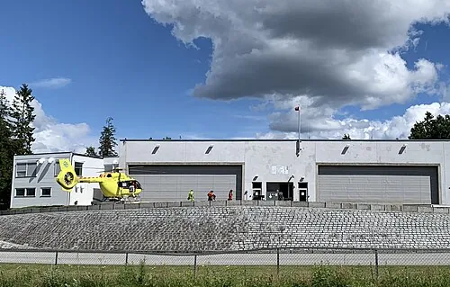 A yellow helicopter parked beside a building and landing area.